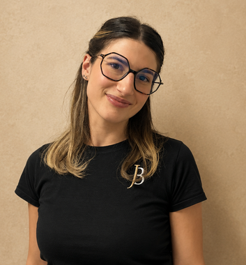 Woman wearing glasses and a black shirt, smiling against a beige wall.