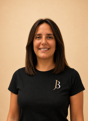 Smiling person in a black T-shirt with a gold “JB” logo against a beige background
