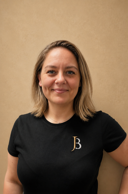 Woman smiling in a black T-shirt with a white logo, standing against a beige wall.