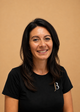 Smiling woman in a black shirt with a white “B” logo against a tan background