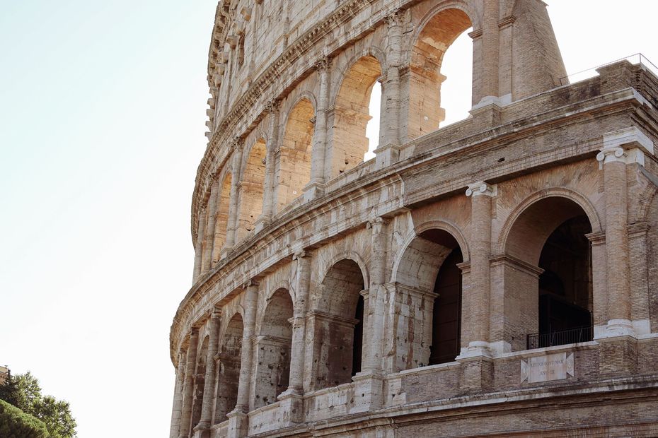 Colosseum in Rome beside a curved street, with buildings and trees under a clear sky