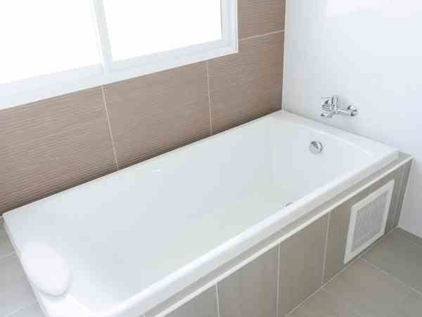Modern white bathtub in a tiled bathroom beneath a window