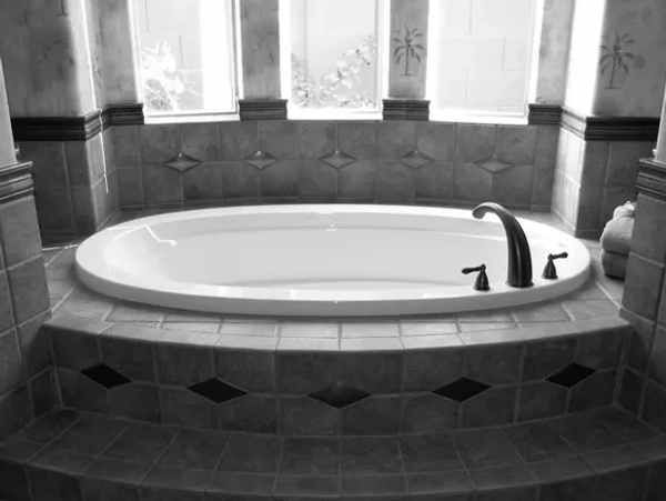 Oval bathtub in a tiled bathroom with a window and a black faucet