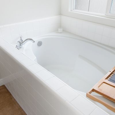 White bathroom with a built-in tub, chrome faucet, and a wooden bath tray on the rim.