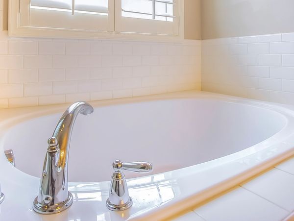 White bathtub in a bright tiled bathroom under a window