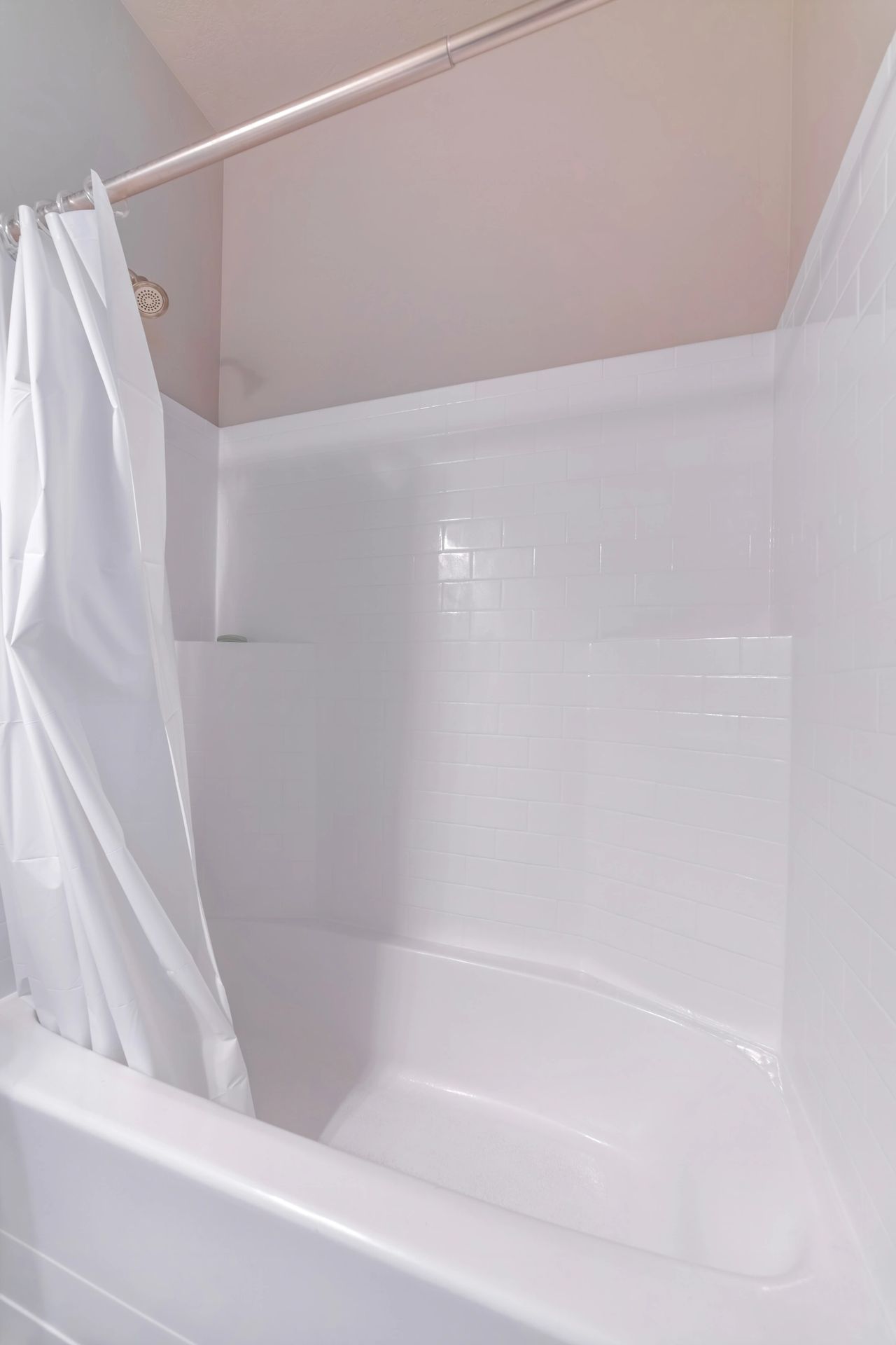 White shower stall with a curved tub and partially open curtain in a bathroom.