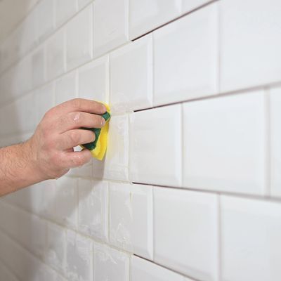 Hand scrubbing white tiled wall with a yellow sponge