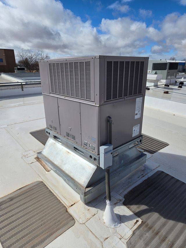 Rooftop HVAC unit with vents and ductwork on a snowy roof under a cloudy sky
