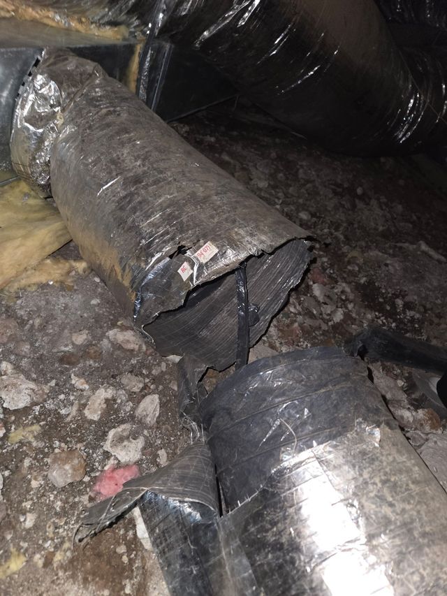 Damaged black insulated duct pipe broken near the floor amidst debris and rough ground