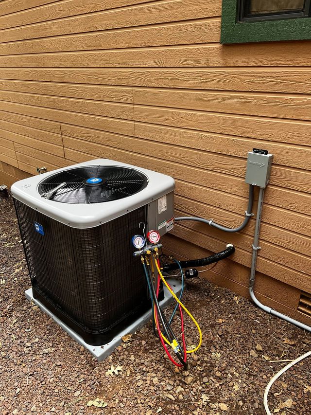 Outdoor HVAC unit beside a brick wall with service gauges and hoses attached