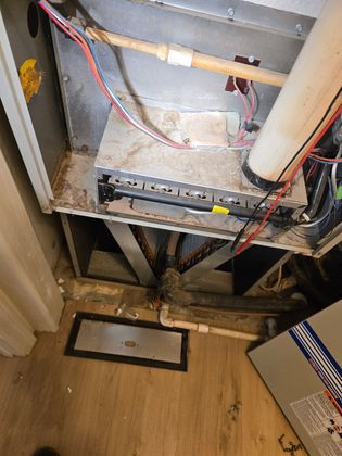 Open HVAC unit with exposed wiring and ducts above a floor vent in a utility space