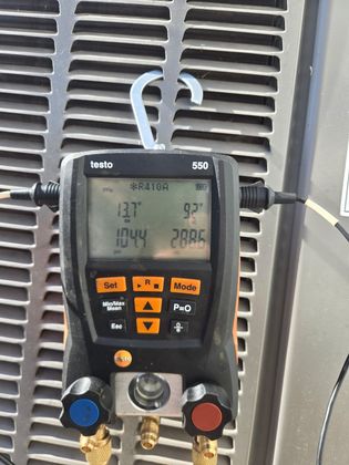 Digital HVAC gauge manifold with display and colored hoses attached to a metal vent grille.