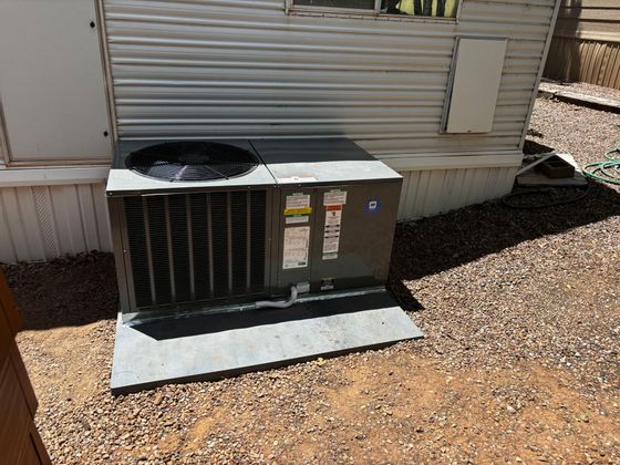 Outdoor HVAC unit beside a beige mobile home on a gravel lot