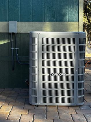 Outdoor air conditioner unit against a green wall and stone facade on a paved patio.