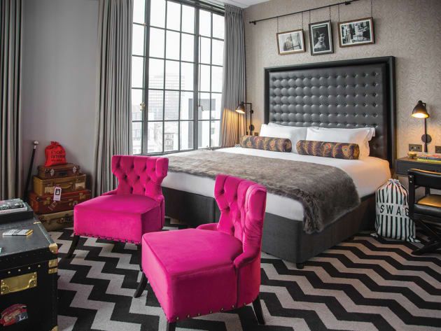 A bedroom with a large bed and two pink chairs