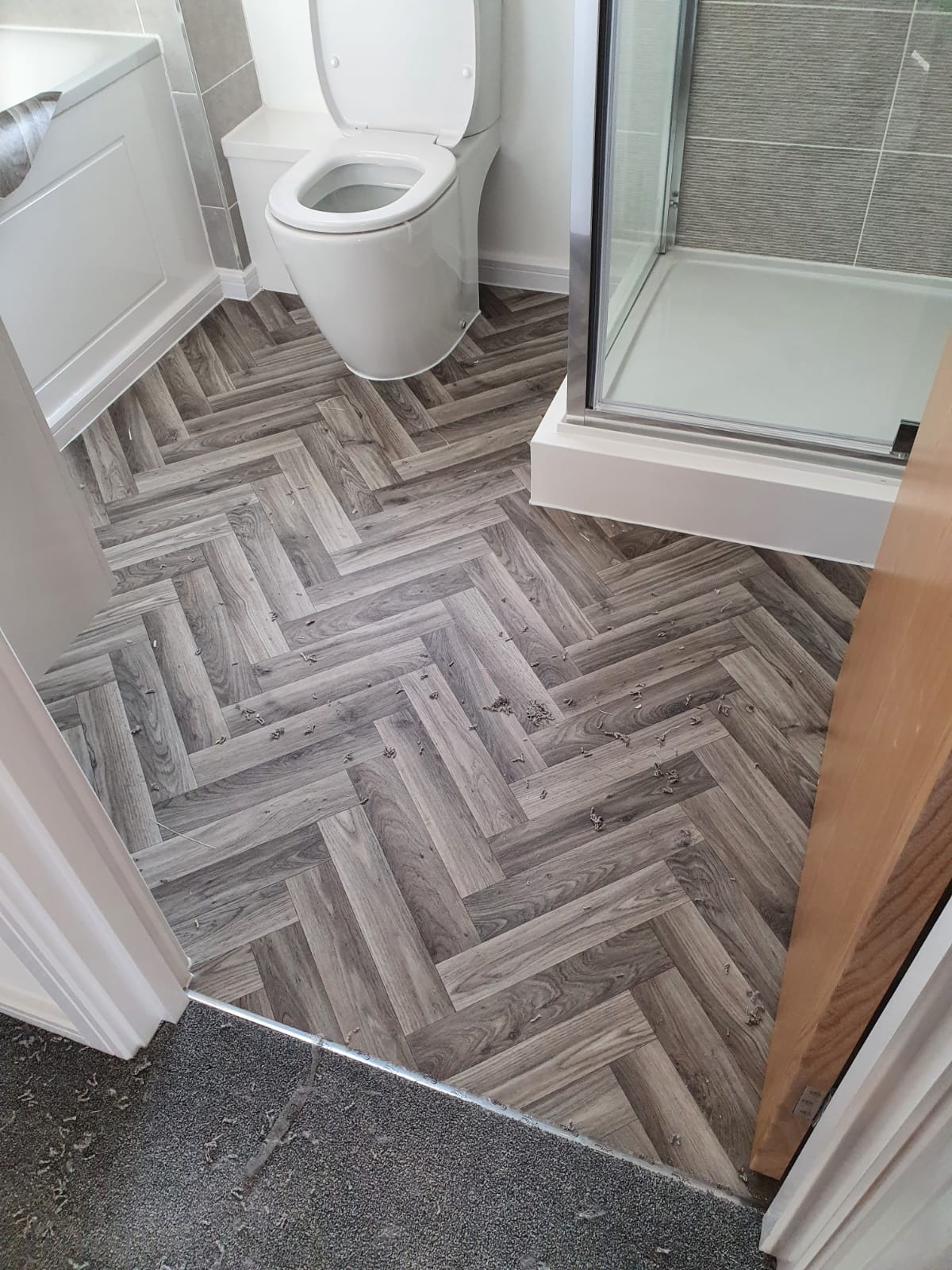A bathroom with a toilet , shower and a herringbone floor.