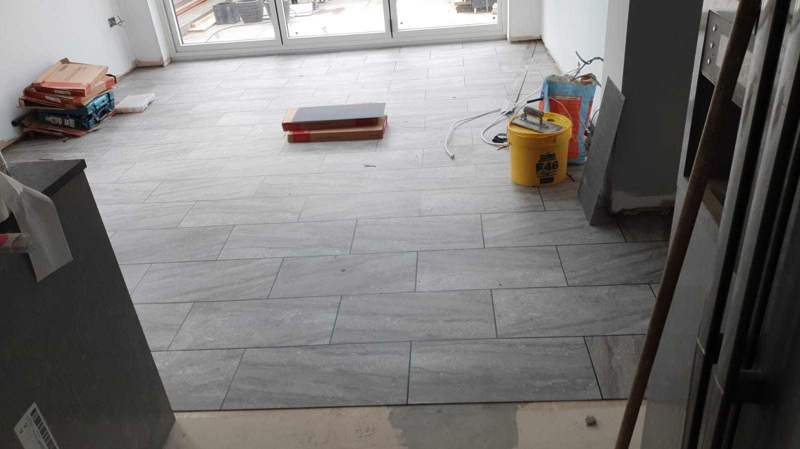 A room with a tiled floor and a yellow bucket on the floor.