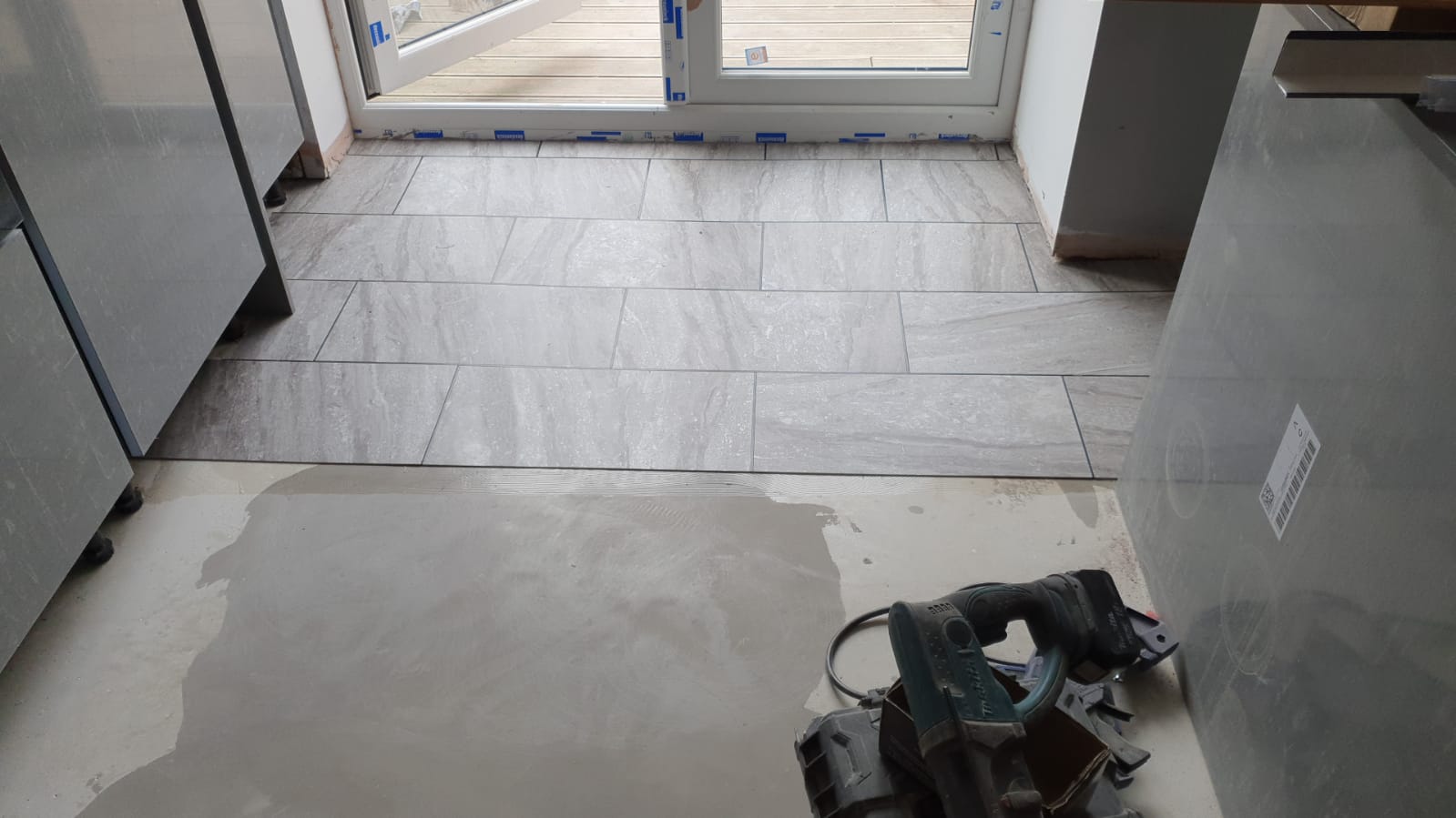A drill is sitting on a tiled floor in a kitchen.