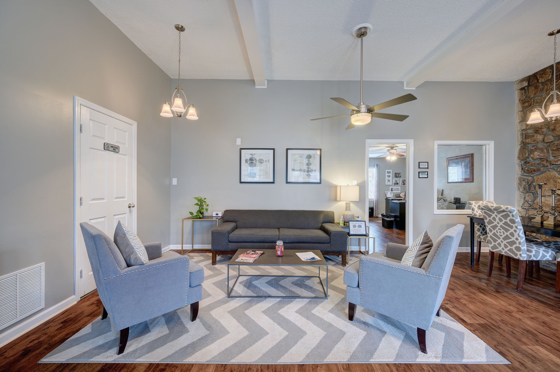 A gray-toned living room featuring a sofa, two armchairs, a geometric rug, and a stone accent wall.