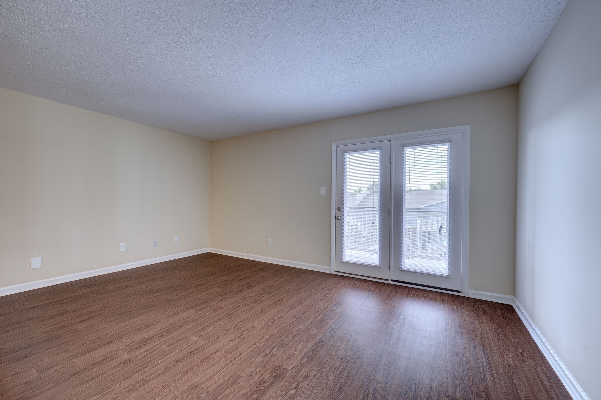 Empty room with light walls and brown wood-look flooring, featuring a set of French doors leading to a balcony.