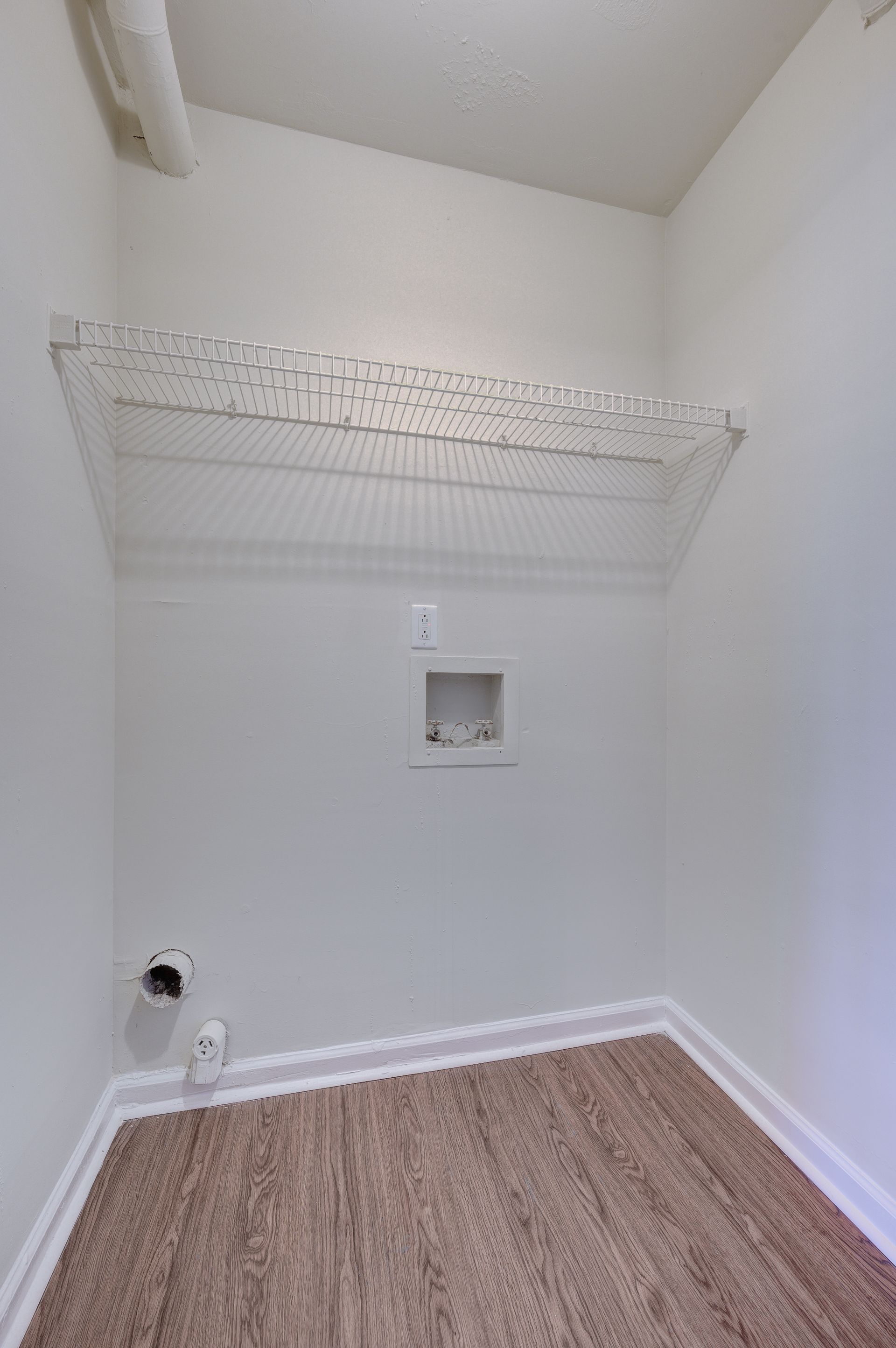 Empty laundry closet with white walls, carpeted floor, wire shelving, and connections for a washer and dryer.