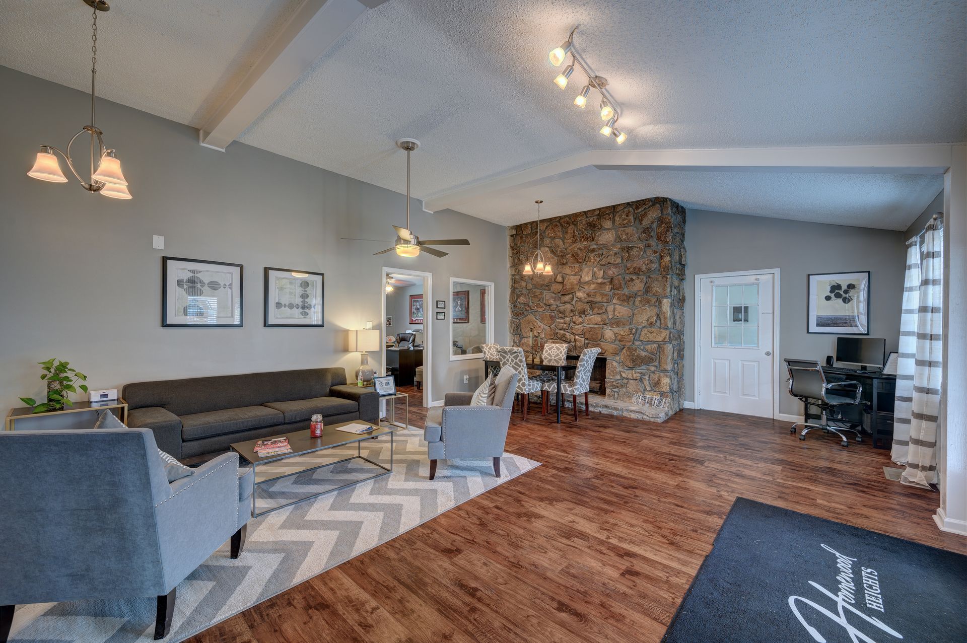 A bright, open living room with gray walls, wood floors, a stone fireplace, gray sofa, armchairs, and office area.
