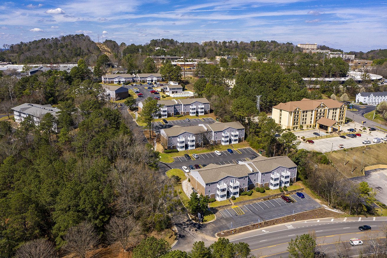 Aerial view of several multi-story apartment buildings nestled among trees with parking lots and a winding road.