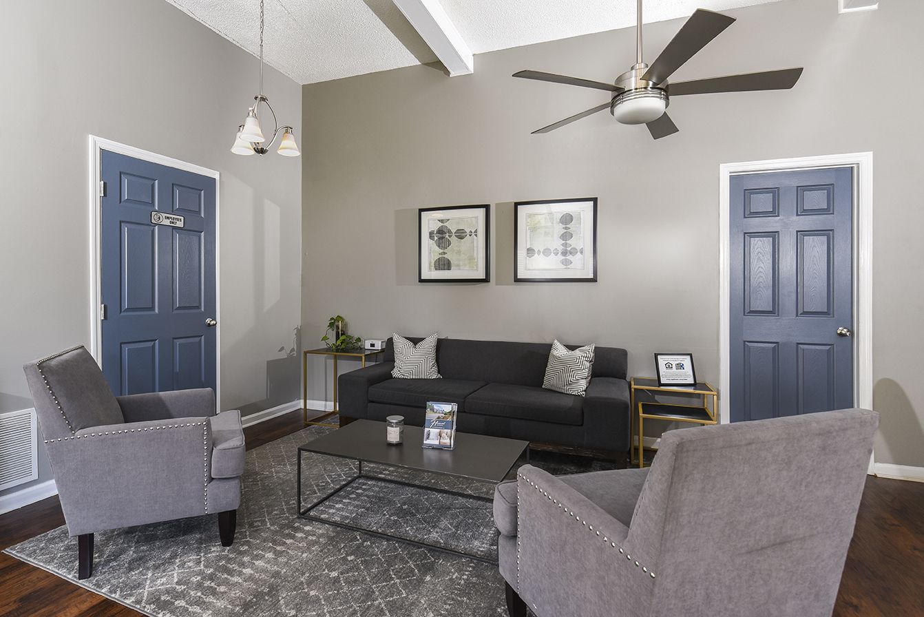 A living room with a dark grey sofa, two armchairs, a coffee table, and blue doors on a light-colored wall.