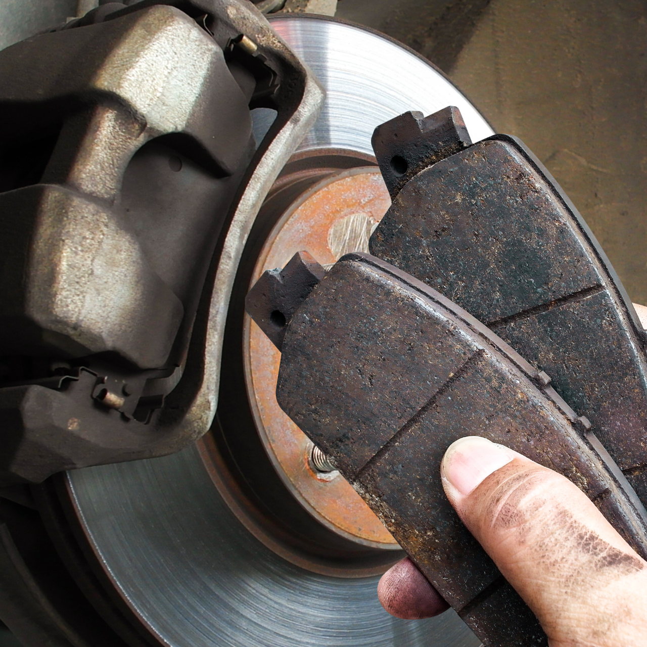 Hand holding a worn brake pad near a car brake rotor and caliper