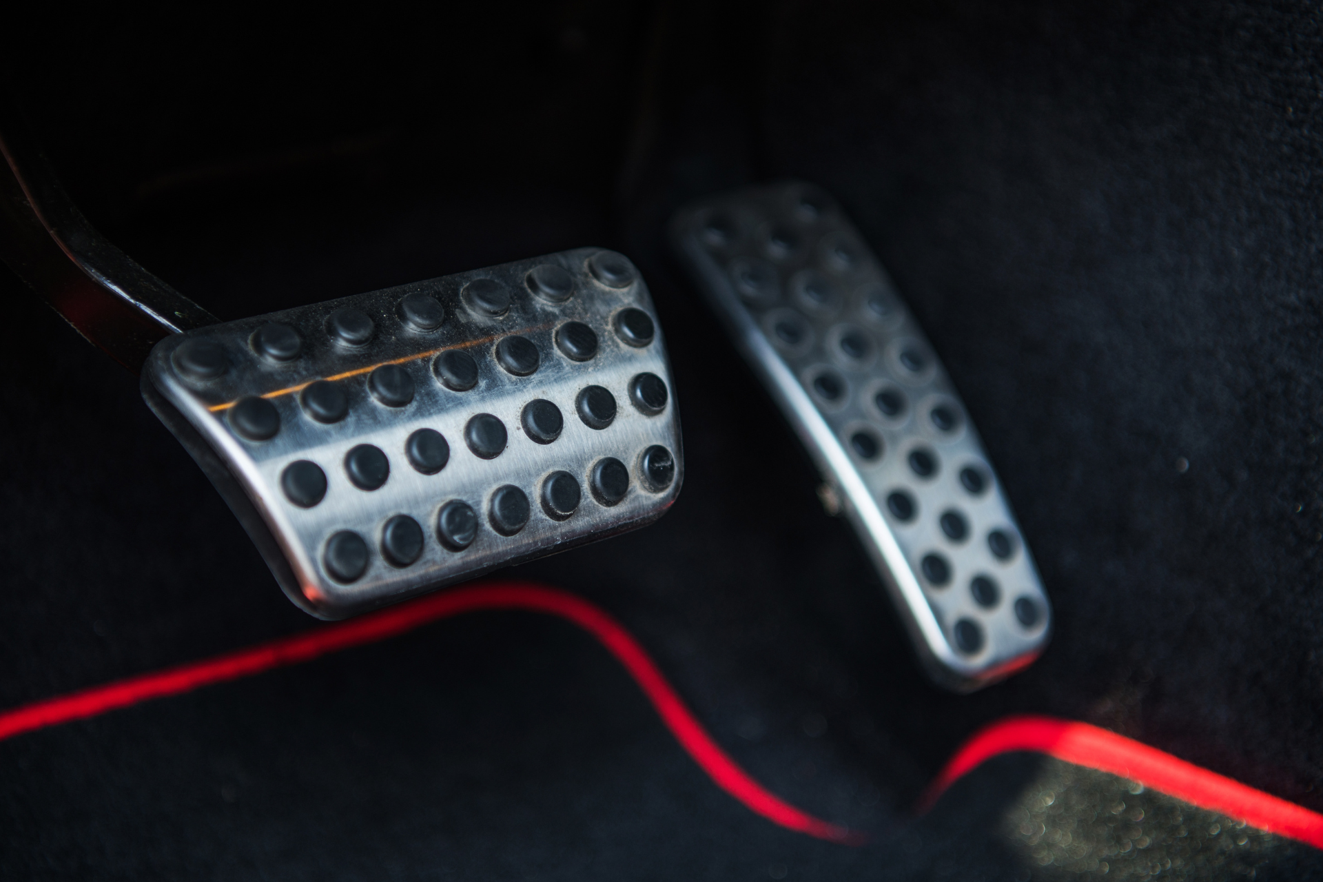 Close-up of a car’s metal pedals on a dark floor mat with a red trim line