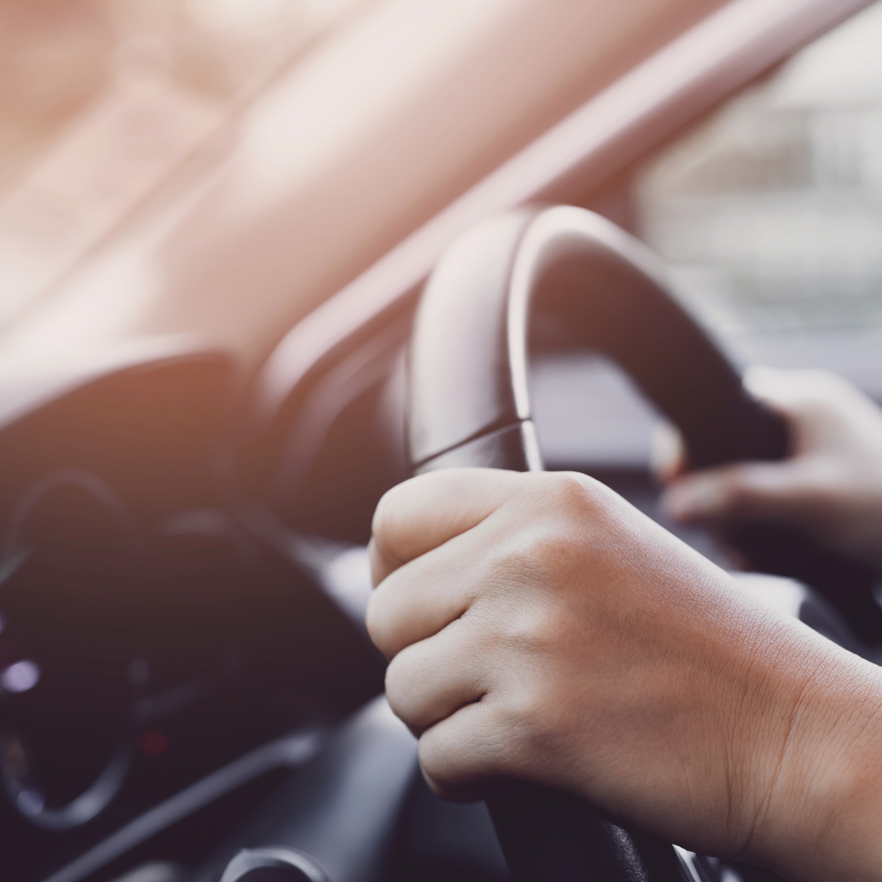 Hands gripping a steering wheel inside a car, with warm sunlight through the windshield