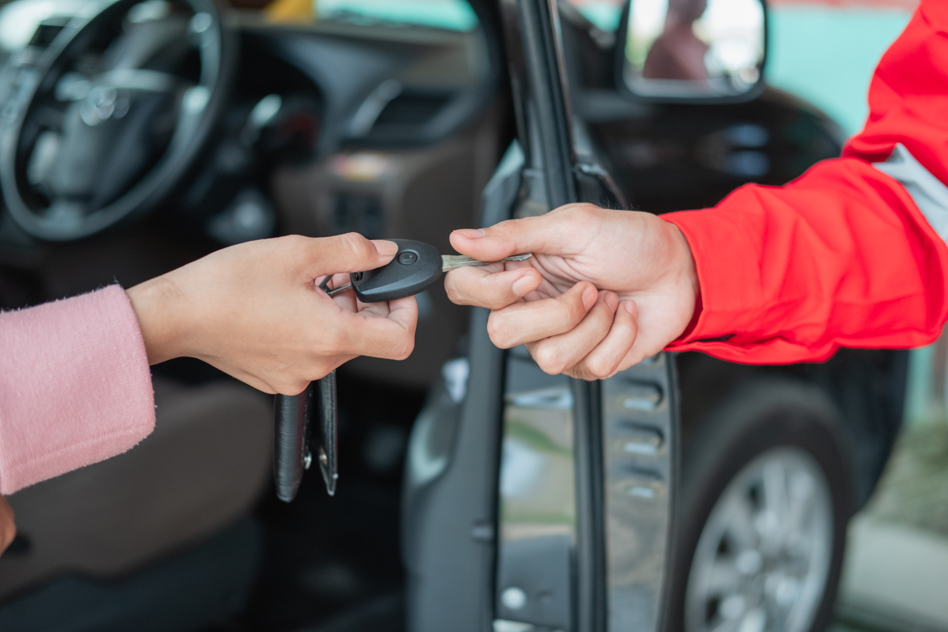 Car keys being handed between two people beside a black car