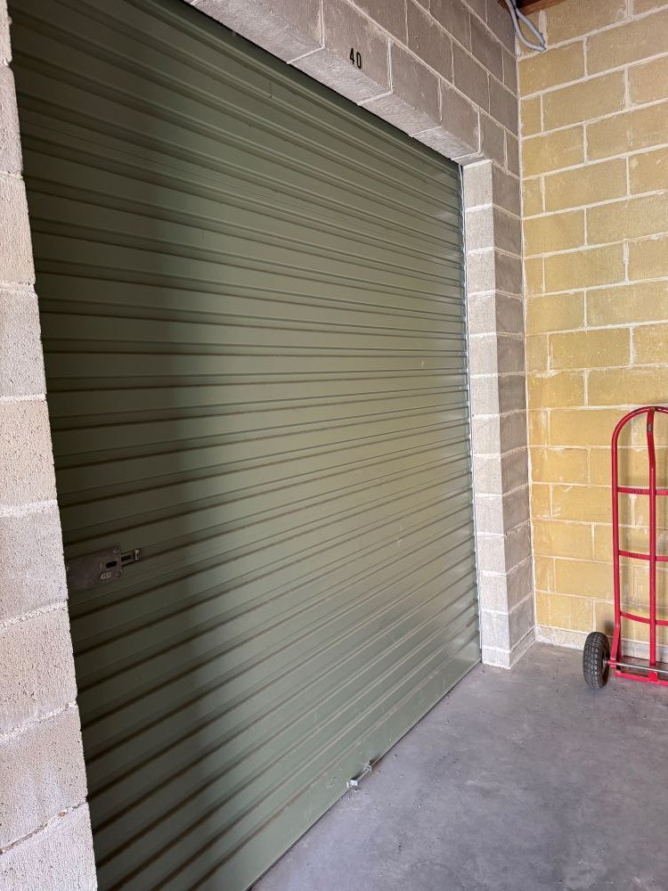 A Green Garage Door is in a Brick Building Next to a Red Dolly — Huskisson Self Storage in Huskisson, NSW
