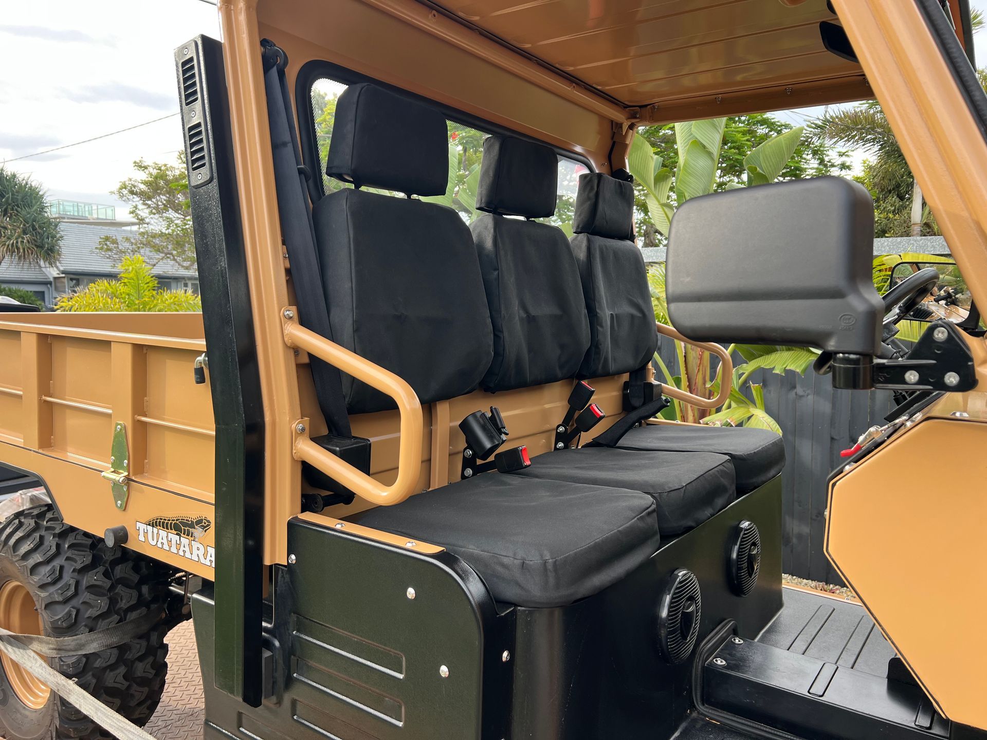 Tan utility vehicle with three black seats and a cargo bed in an outdoor setting.