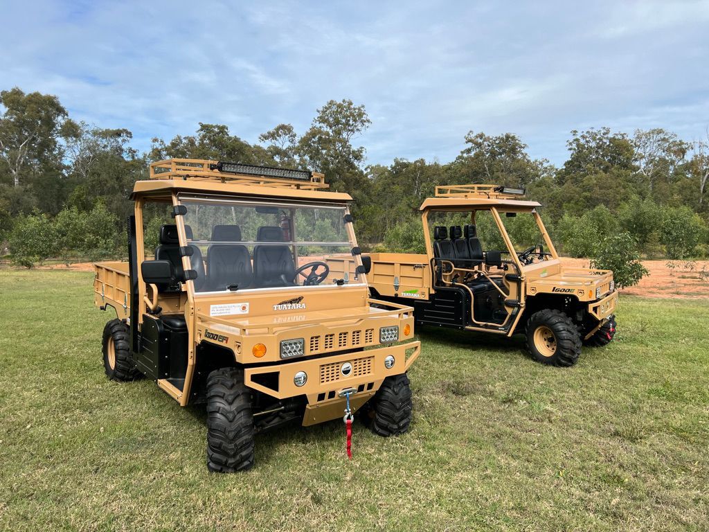 Two tan off-road utility vehicles parked on a grassy field with trees in the background.