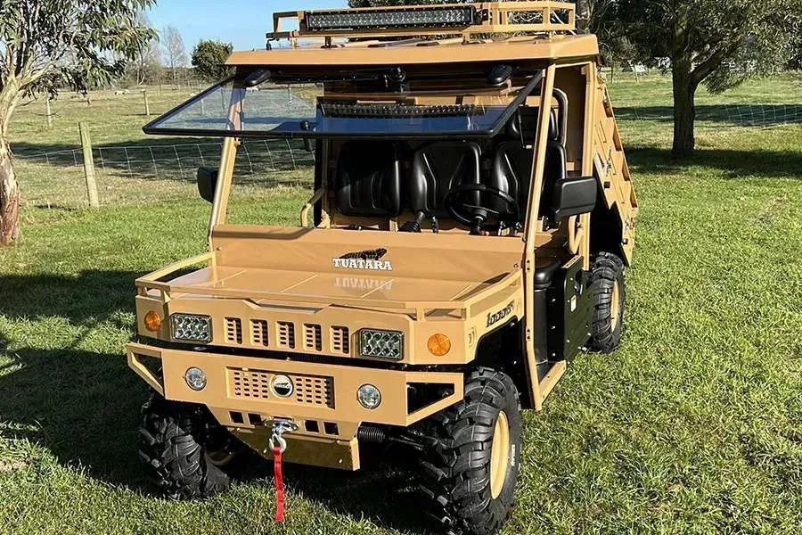 Tan utility terrain vehicle with a front winch, roof rack, and LED lights, parked on a grassy field.