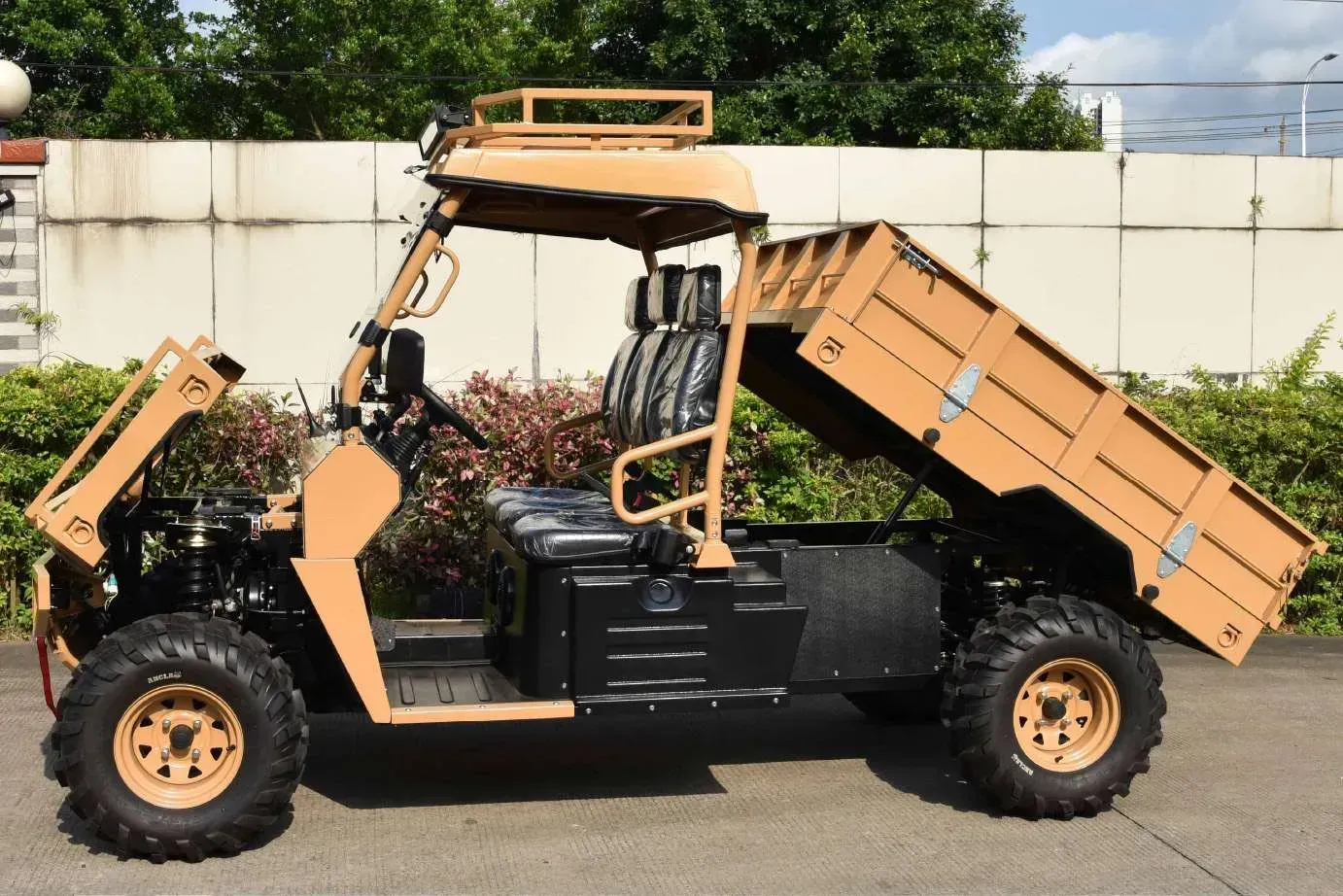 A tan off-road utility vehicle with a lifted cargo bed parked outdoors against a concrete wall.