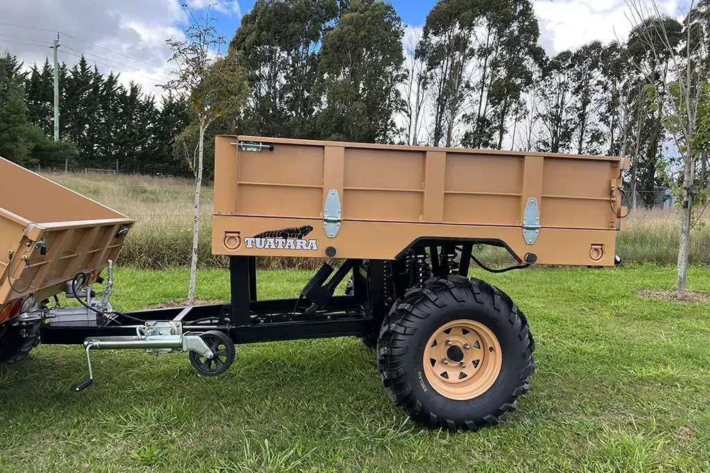 Tan-colored farm utility trailer with large, heavy-duty tires parked on a grassy field.