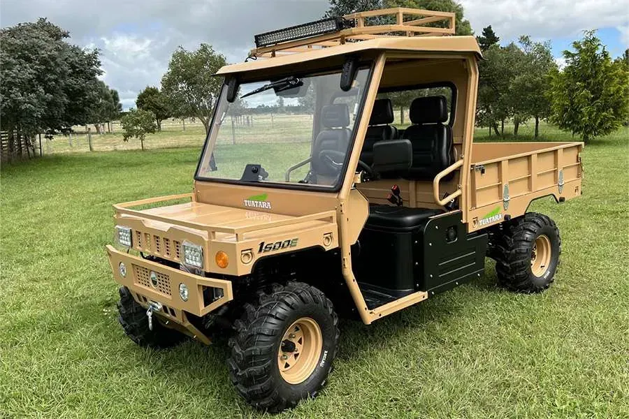 A tan, rugged utility vehicle with a cargo bed parked on a grassy field under a cloudy sky.