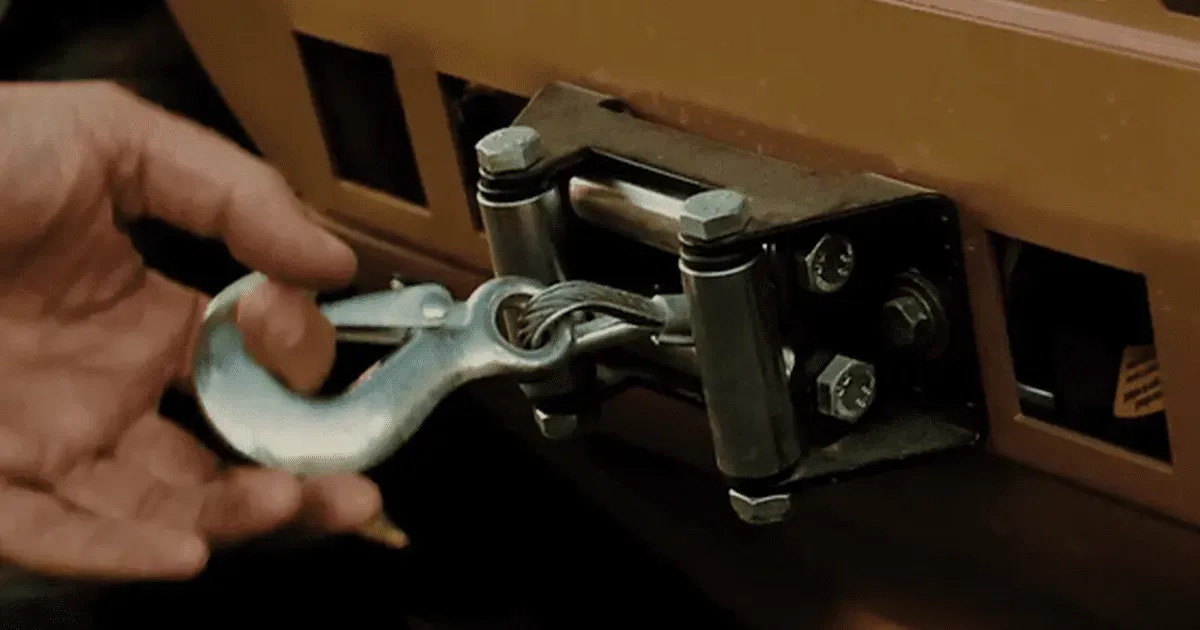 A hand holds a metal winch hook attached to a roller fairlead mounted on a vehicle bumper.