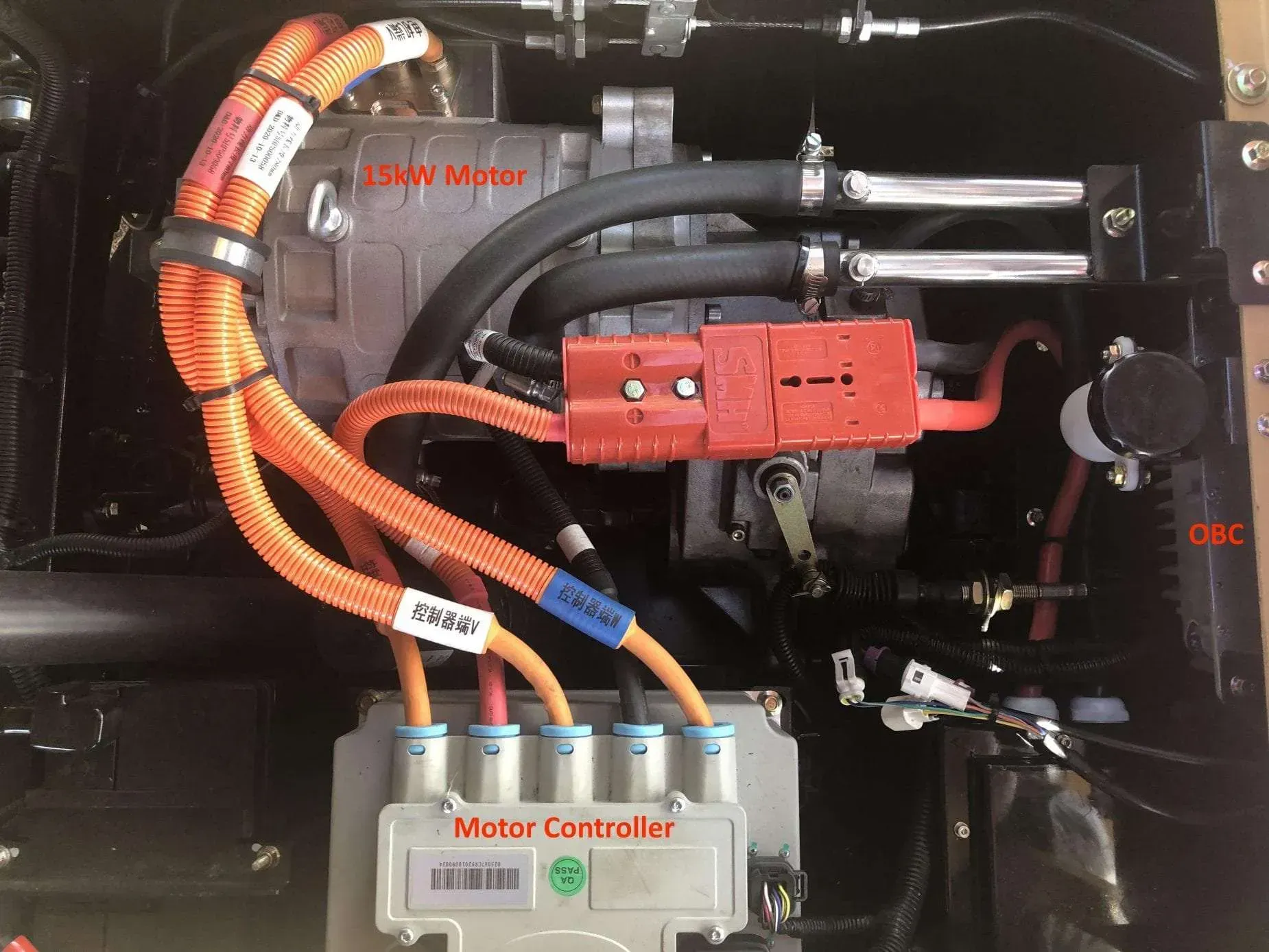 A top-down view of an electric vehicle powertrain, featuring a 15kW motor, motor controller, and orange high-voltage cables.