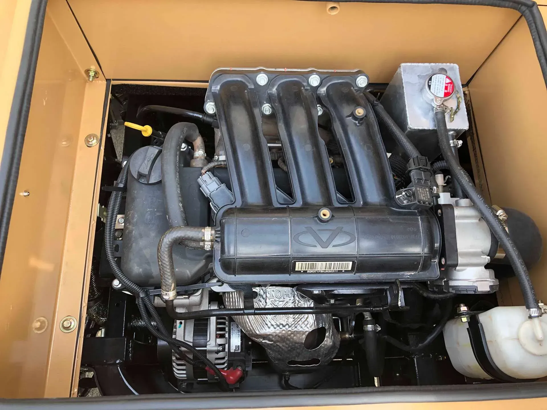 A high-angle view of a clean 4-cylinder engine mounted inside a tan, rectangular metal frame or enclosure.