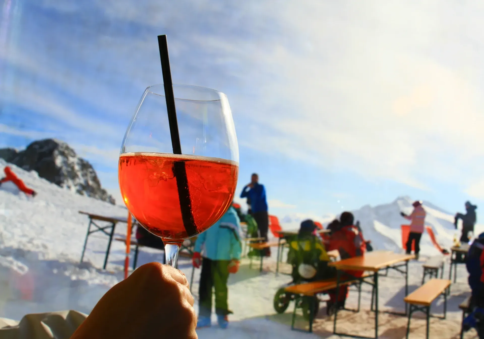 Hand holding a red drink with a straw at a snowy outdoor ski lodge, people in the background