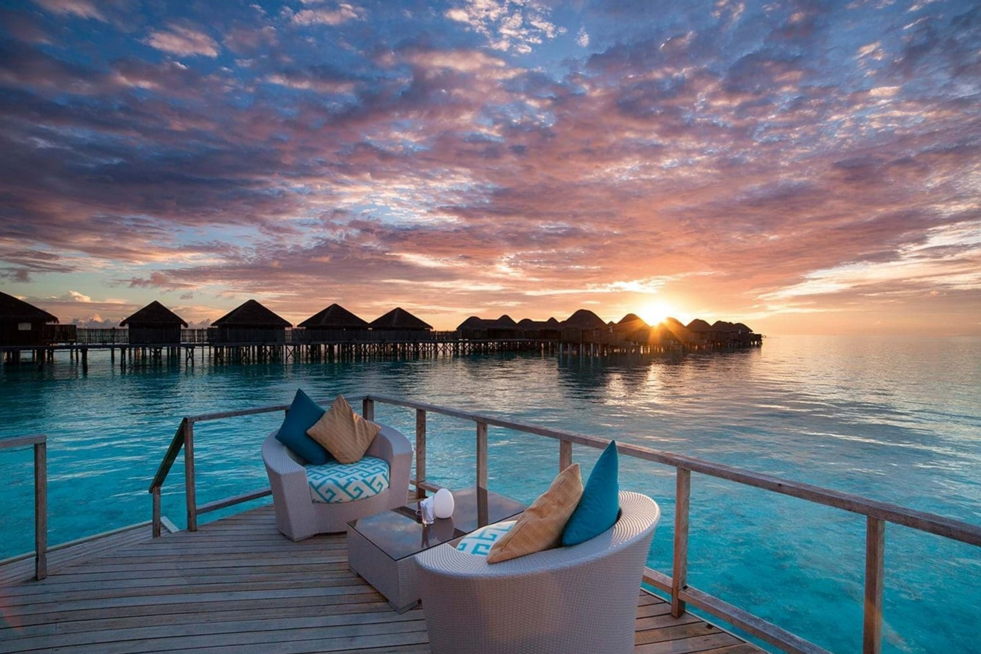 Two chairs are sitting on a deck overlooking the ocean at sunset.