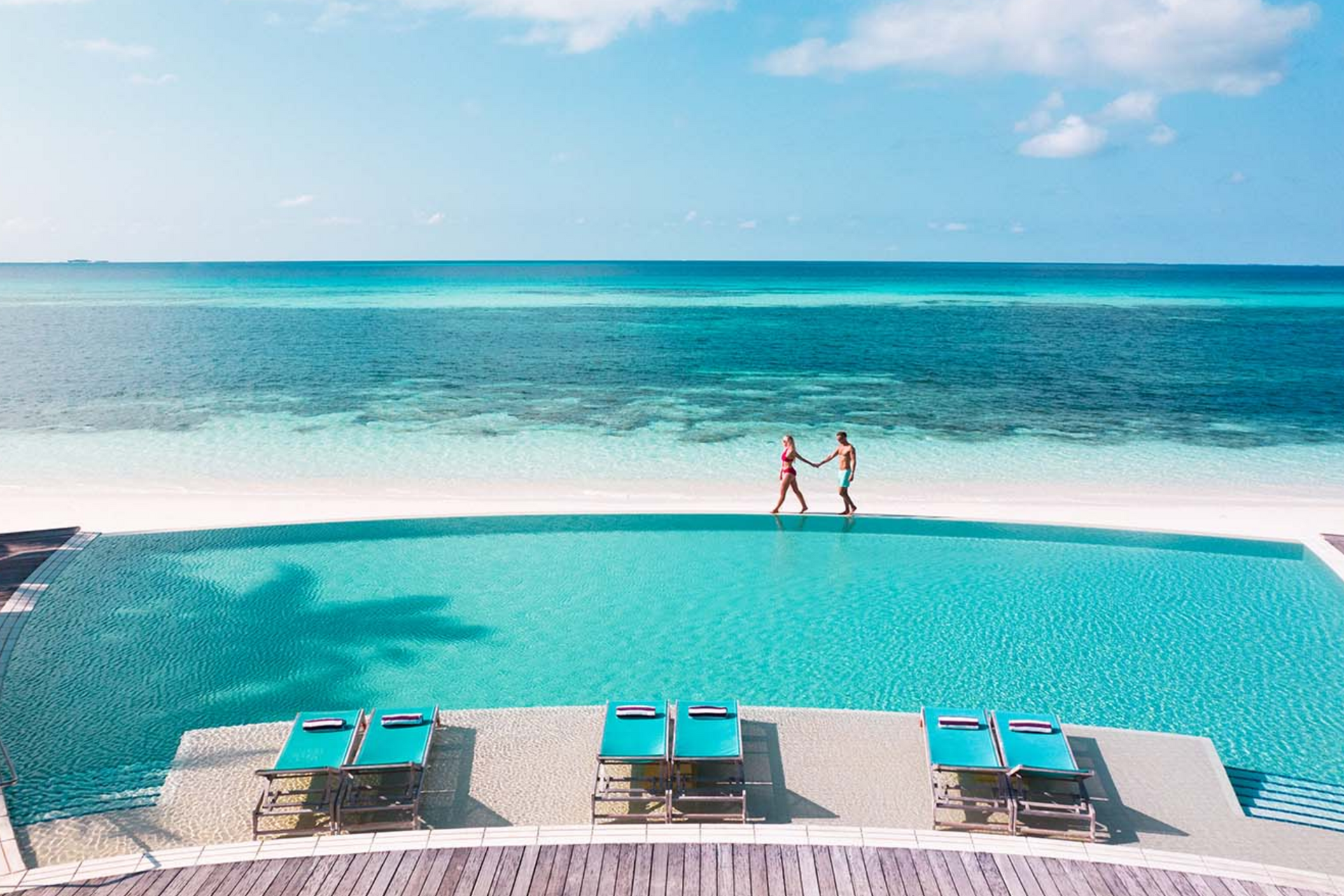 A couple is standing next to a swimming pool on a beach.