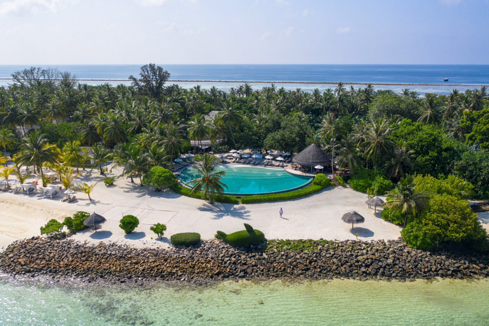 An aerial view of a tropical island with a large swimming pool surrounded by palm trees.