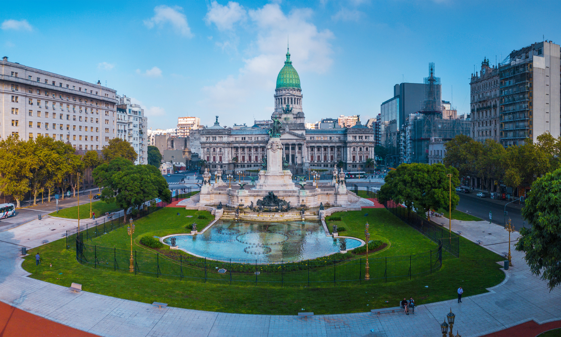A large building with a dome and a fountain in front of it in a city.