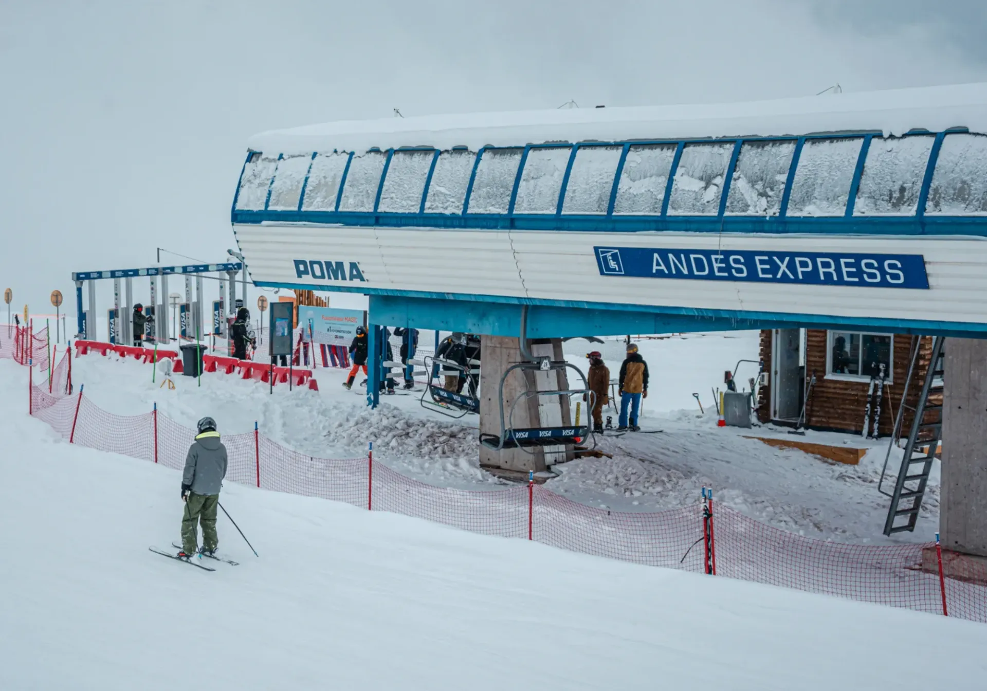 Ski lift station at a snowy mountain resort with blue canopy and people waiting near the entrance.