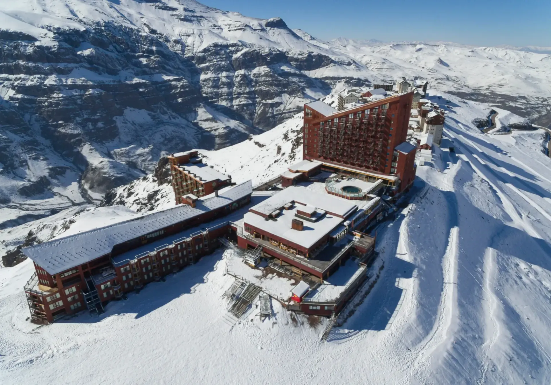 Snow-covered mountain resort with several lodge buildings and ski slopes under bright sunlight