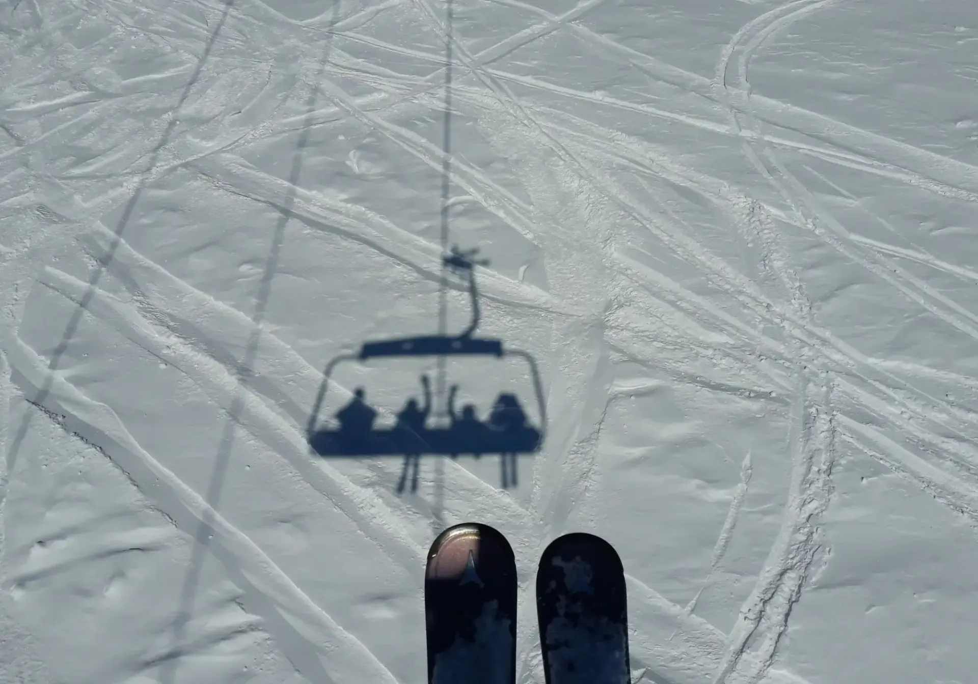 Ski lift shadow on snow with boots visible at the bottom of the frame.